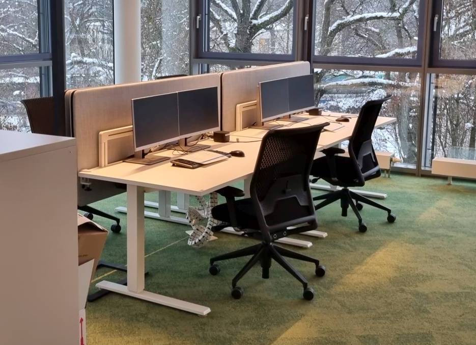 Ein Büro mit zwei Schreibtischen und zwei Monitoren vor einem Fenster.